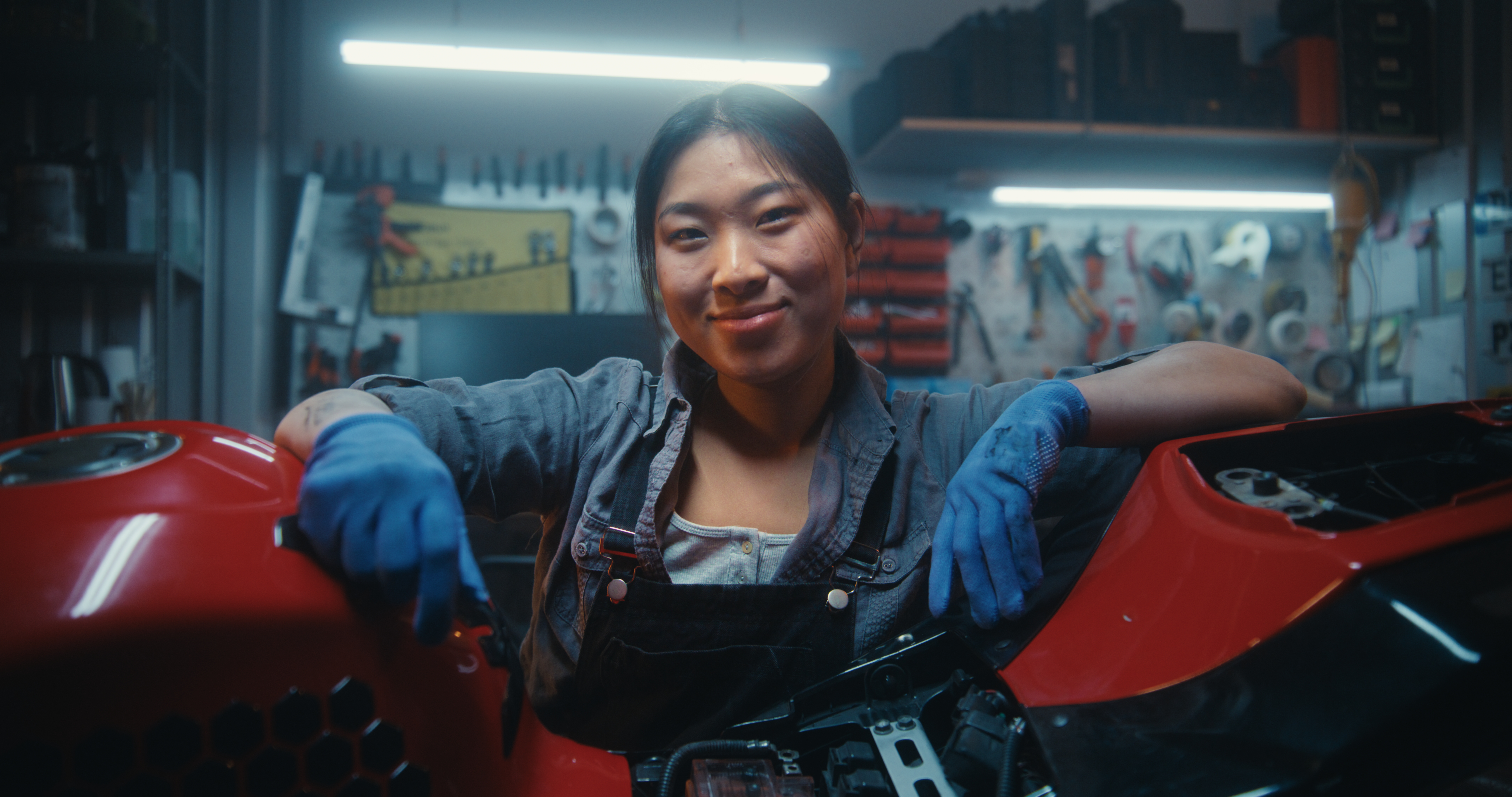 Portrait of Happy Smiling Female Mechanic Leaning on Motorcycle After Successful Repair. Young Asian Woman Satisfaction After Finishing Technical Maintenance and Electronics Repair in Garage Workshop.